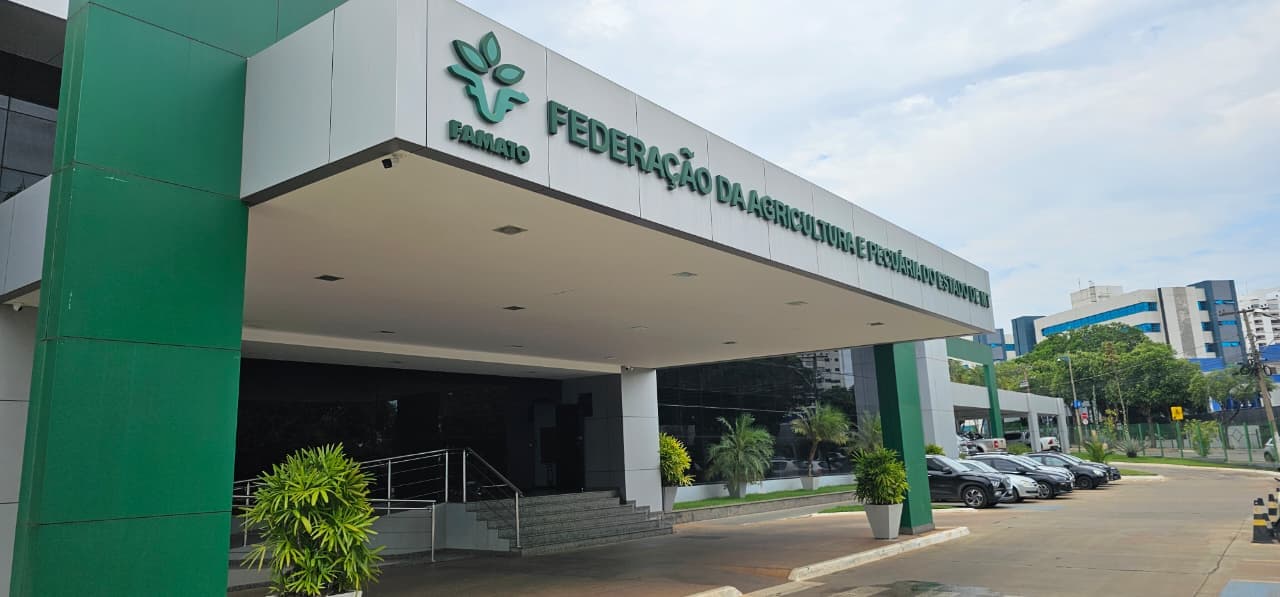 Fachada do prédio da Famato com pilares verdes, letreiro da federação e estacionamento ao fundo.